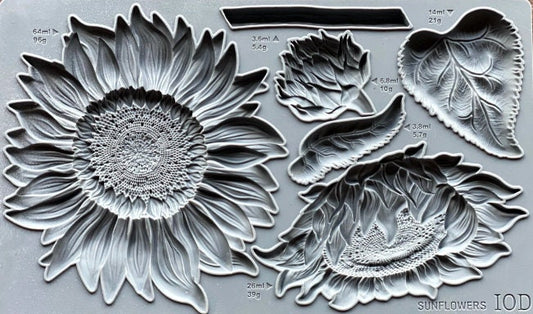 May include: A silicone mold for baking or crafting. The mold features a large sunflower design with a detailed center and petals. There are also smaller sunflower designs, leaves, and bud shapes. The mold is gray and has measurements and weights printed on it. The text on the mold reads 'SUNFLOWERS IOD'.